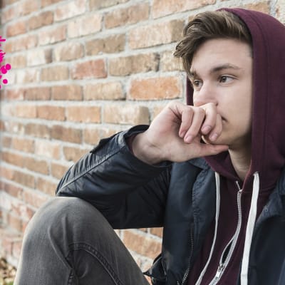 en ung man som sitter ute och lutar mot en vägg och ser bekymrad ut