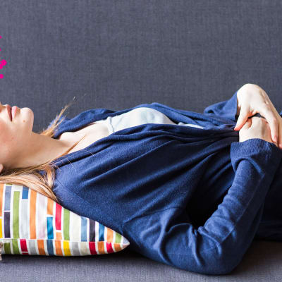 en vuxen kvinna som ligger på en soffa med sina händer placerade på sin nedre mage