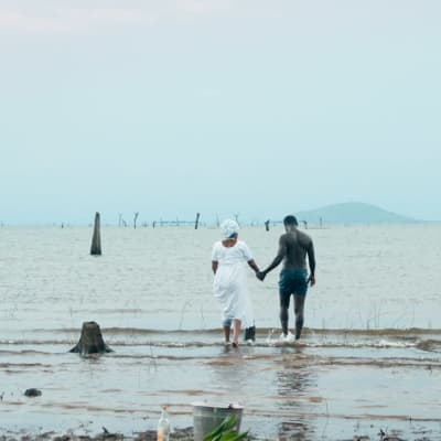 Mies ja nainen seisovat meressä käsi kädessä