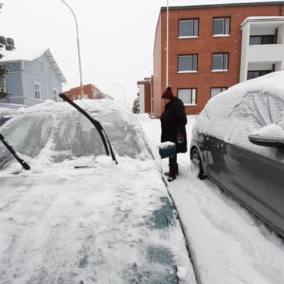 Nainen puhdistaa autoa lumesta. 