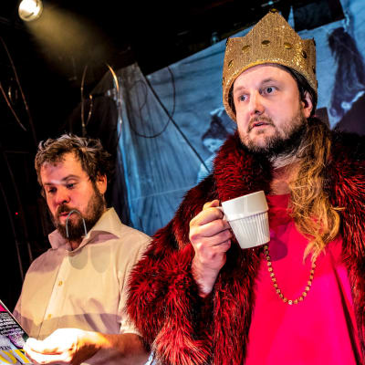 Antti Mankosen näyttelemä Jussi lukee Anna-lehteä. Vieressä seisoo kahvikuppi kädessään ja kruunu päässään Pekko Käpin näyttelemä kuningatar Kristiina.