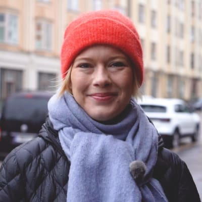 Ekonomen Heidi Schauman står ute på en regnig gata i Tölö i Helsingfors, ler och tittar in i kameran. 