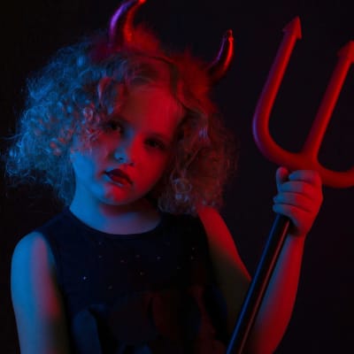 Pieni tyttö ob pukeutunut paholaiseksi, päässä on sarvet ja kädessä leikkihiilihanko.