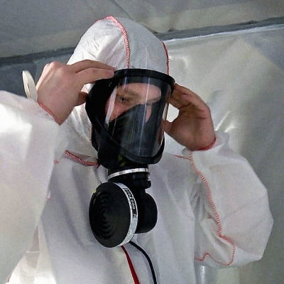 Rakennustyömies pukee suojapuvun ja hengityssuojaimen asbestityömaalla.