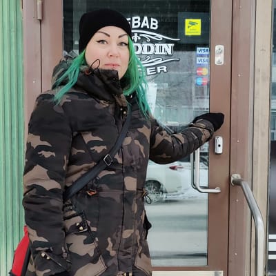 Yrittäjä Laura Johansson seisoo Kebab- ja hampurilaisravintolansa etuovella.