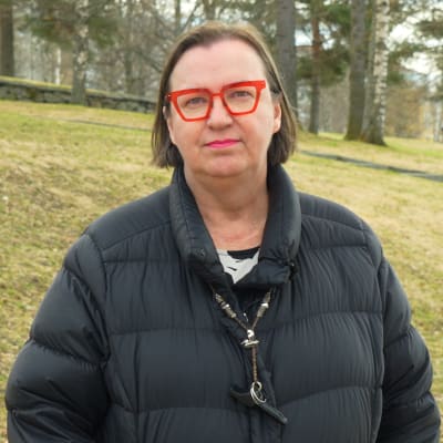 Anne Sid-Koskela har röda glasögon och svart dunjacka. Hon står i en park i Vasa.