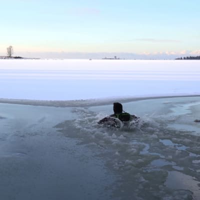 En man har gått genom isen. Endast huvudet och och axlarna syns. Det skvätter vatten runt honom,