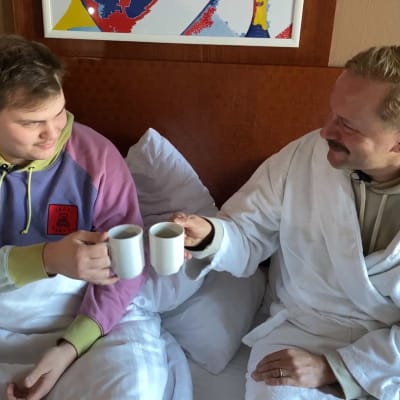 UMK-voittaja Aksel Kankaanranta hotellihuoneen sängyssä aamiaisella kylpytakkiin pukeutuneen Mikko Silvennoisen kanssa.