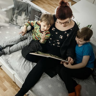 Ylhäältä kuvattu, nainen lukee lapsille sohvalla kirjaa.