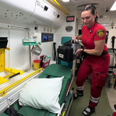 Naispuolinen ensihoitaja siirtää ambulanssin sisällä sydäniskuria eli defibrillaattoria.