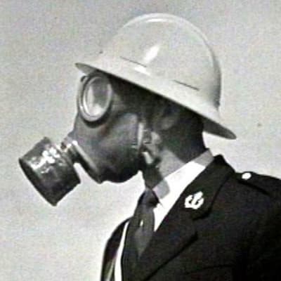 Poliisiupseeri kaasunaamarissa ja kypärässä Lahden messujen väestönsuojelunäytöksessä 1969.