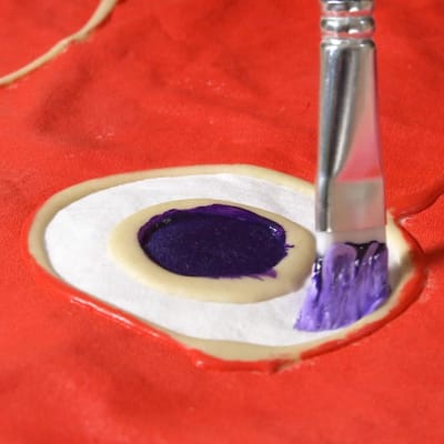Karpfiskens öga målas med pensel på textil.