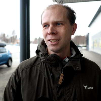 En mans ansikte. I bakgrunden parkeringsplats.