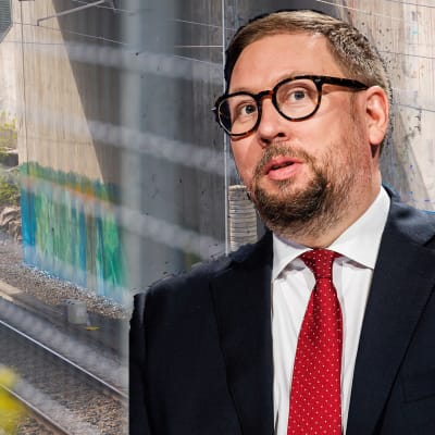 Kollage med Paavo Arhinmäki som iklädd kostym står framför en graffitimålning på en tunnelvägg.