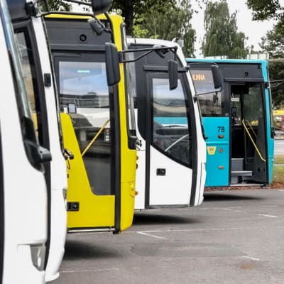 Fyra bussar i olika färger står uppradade på en busstation i Tavastehus. 
