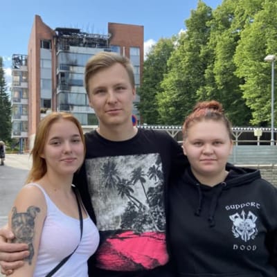 Eerika Pasanen, Samu Silventoinen och Sari Veijalainen står framför ett flervåningshus som brunnit 
