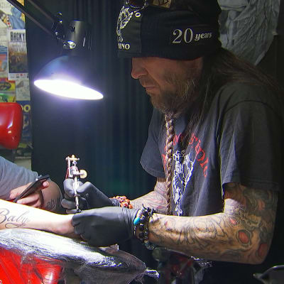En man i skägg gör en tatuering på baksidan av en annan mans hand. 