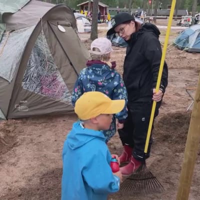 Nainen juttelee lapsen kanssa telttojen edustalla Pitkis-Sport-leirillä. Kuvan etualalla on myös toinen lapsi.