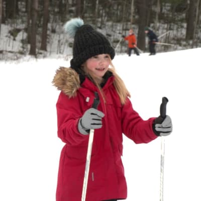 Barn lär sig att åka skidor i Åbo och vi ser en pojke i brungrå rock samt en flicka i en röd rock.