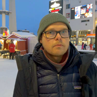 Valotaiteilija Jukka Huitila seisoo Rovaniemen ydinkeskustassa mainosvalojen ympäröimänä.
