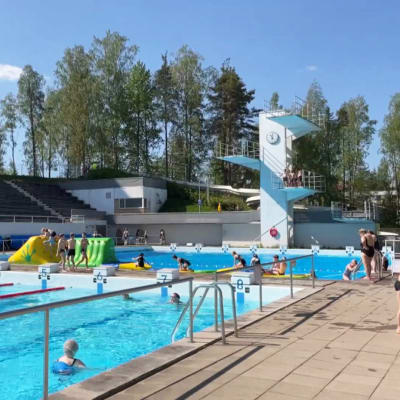 Yleiskuva Riihimäen maauimalasta. Etualalla isossa altaassa vesuijuoksija. Taempana lapsia ilmatäytteisellä temppuradalla. Taka-alalla hyppytornit. Vitosessa on ruuhkaa.