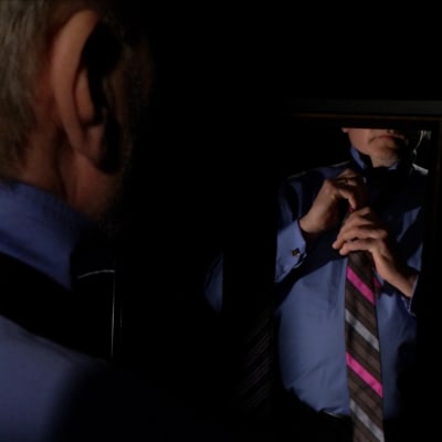 Anonyymi mies solmii solmiota peilin edessä dramaattisesti valaistuna.