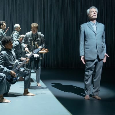 David Byrne ja orkesteri lavalla, harmaissa puvuissa paljain jaloin, kuva konserttielokuvasta David Byrne's American Utopia.