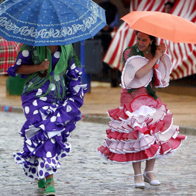 Flamencoasuiset naiset rientävät sateenvarjojen alla feria-alueella Sevillassa.