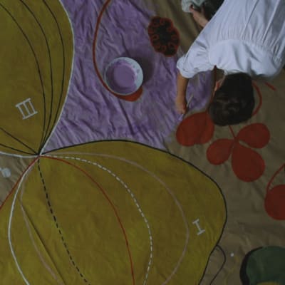 bild uppifrån av konstnären som målar ett av sina enorma verk sittande på golvet.
