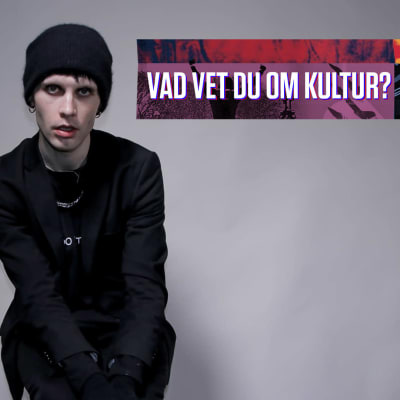 En man med mössa poserar mot grå vägg.