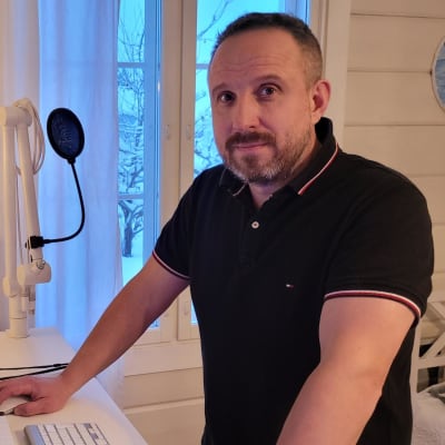 Mies seisoo tietokonepöydän takana ja tekee töitä tietokoneella