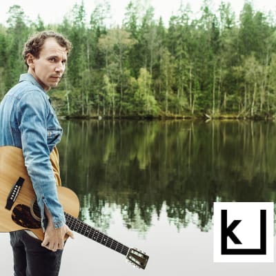 Kirjailija Juha Itkonen kitaran kanssa rannalla