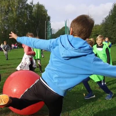 Lågstadiebarn spelar fotboll med gymnastikboll