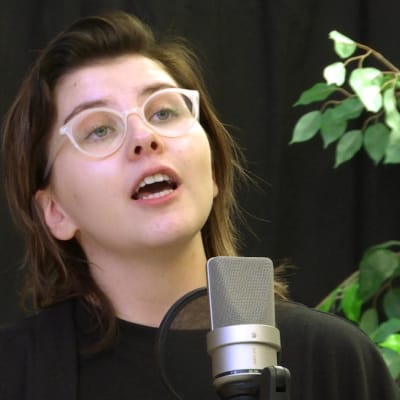 En ung kvinna med glasögon står vid en microfon och rappar.