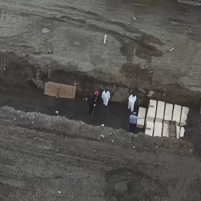 Tiotals kistor begravs av vitklädda arbetare på Hart Island utanför New York.