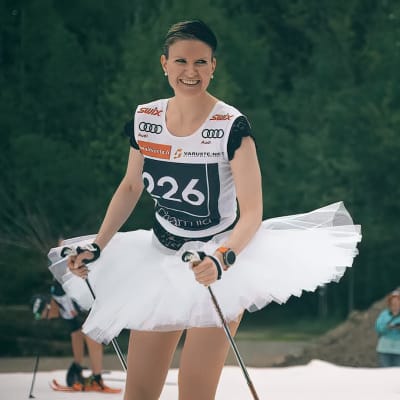 Naishiihtäjä hiihtää ballerina-asussa Supersprintti-kilpailussa vuonna 2022. Taustalla kaksi katsojaa, hiekkakasa ja metsää.