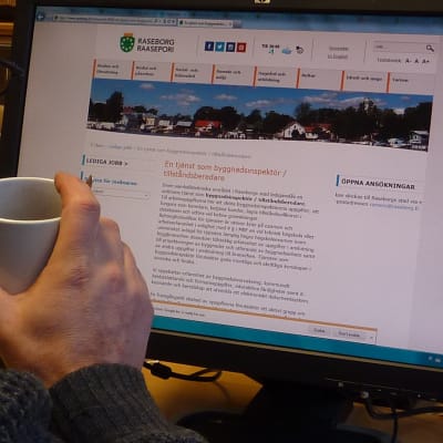 En person som dricker kaffe och tittar på Raseborg stads hemsida.