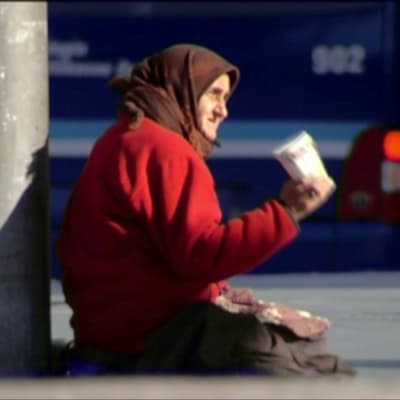 äldre romsk kvinna tigger mitt i trafiken med pappmugg