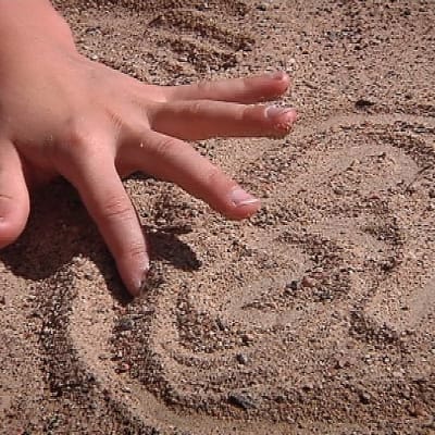 Lapsen sormi piirtää hiekkaan kuvioita. Koulujännitys voi saada lapsen haikailemaan kesäloman huolettomia päiviä.