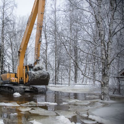 Kuvassa kaivinkone kesämökin pihalla, vasemmalla punainen aitta. Oikealla näkyy mökkiä.