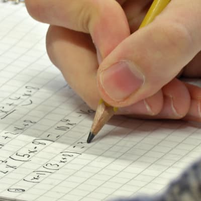 Oppilas kirjoittaa matematiikan tehtävää vihkoon