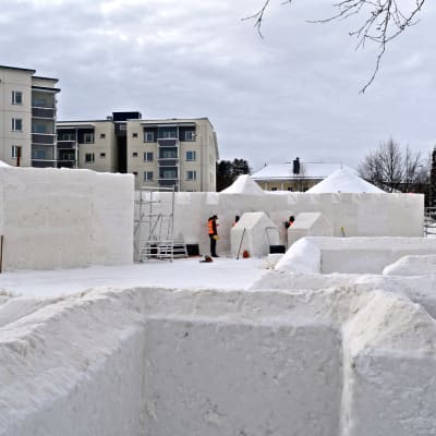 Lumimiilun keskeneräiset lumiseinämät ja lumilinnan rakentajia työssään.