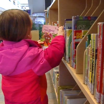 Lapsi etsii kirjaston hyllystä luettavaa.