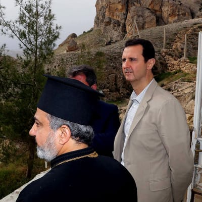 Bashar al-Assad ja kirkon mies tarkastelemassa maisemaa kallion reunalla.