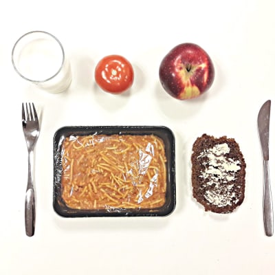 Einesruokalounas, spaghettia, leipä, omena ja tomaatti pöydällä.
