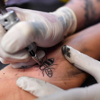 Työmehiläis-aihetta tatuoidaan henkilön käsivarteen. 