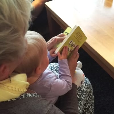 Lapsi lukee kirjaa äitinsä sylissä.