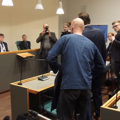Syytetty asettelee takkiaan istuntosalissa oikeudenkäynnin alussa.