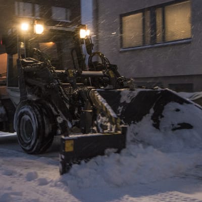 Traktori auraa lunta lumipyryssä.