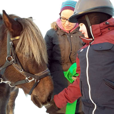 Einari Purra tervehtii terapiahevosta Niiloa. Ratsastusterapeutti Lena Lassila apuna.
